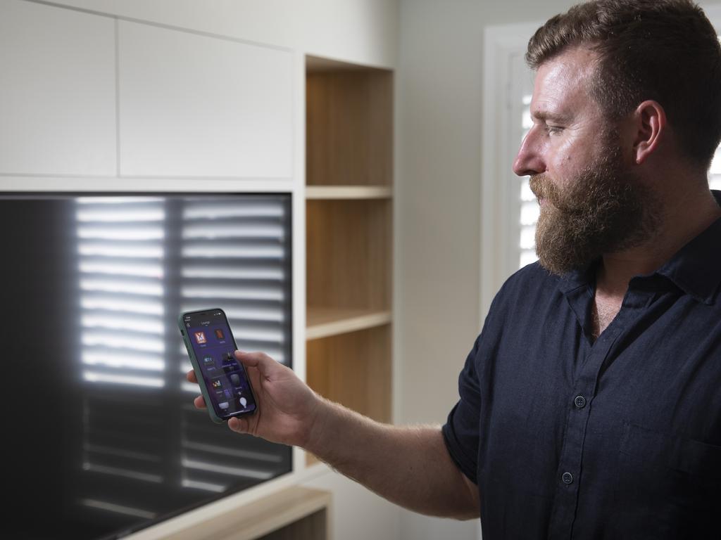 Electronic Living founder holding smartphone with the Control4 app in front of TV screen